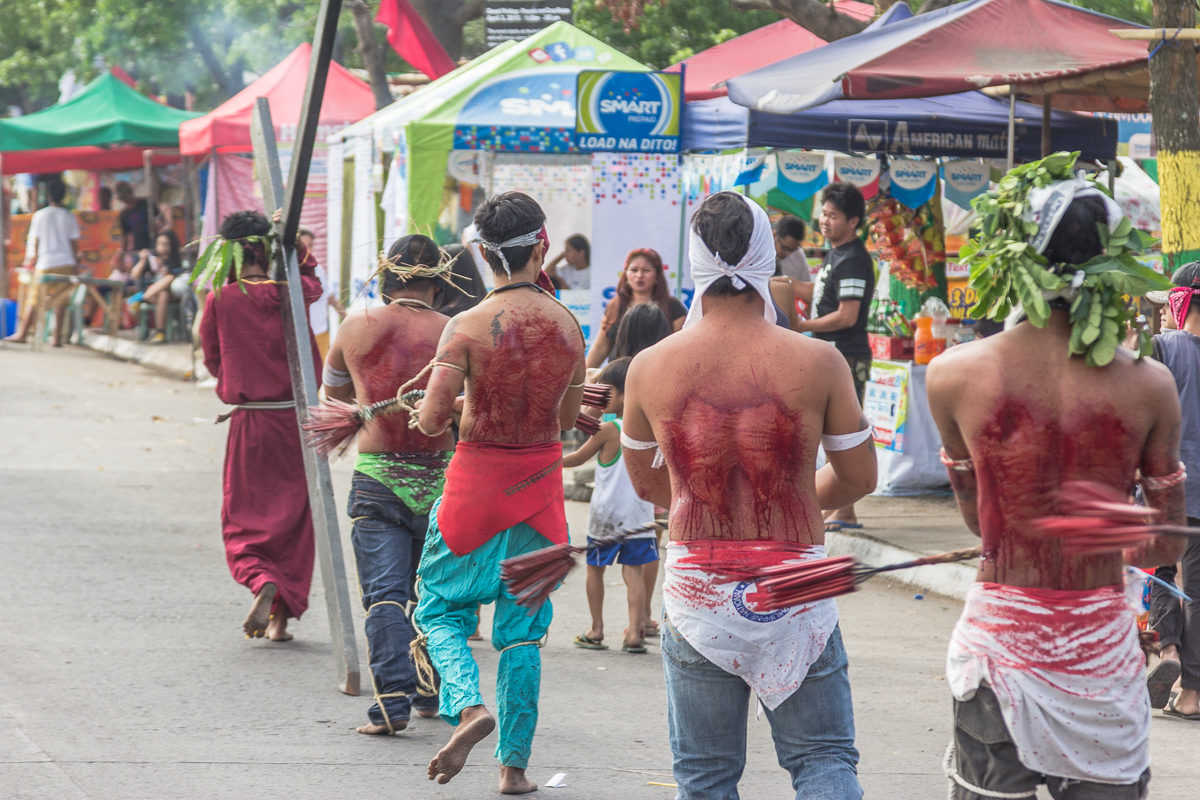 Processie door de straten van Angeles en San Fernando op de Filipijnen, terwijl gemaskerde mannen zichzelf op de rug slaan met houten klossen.