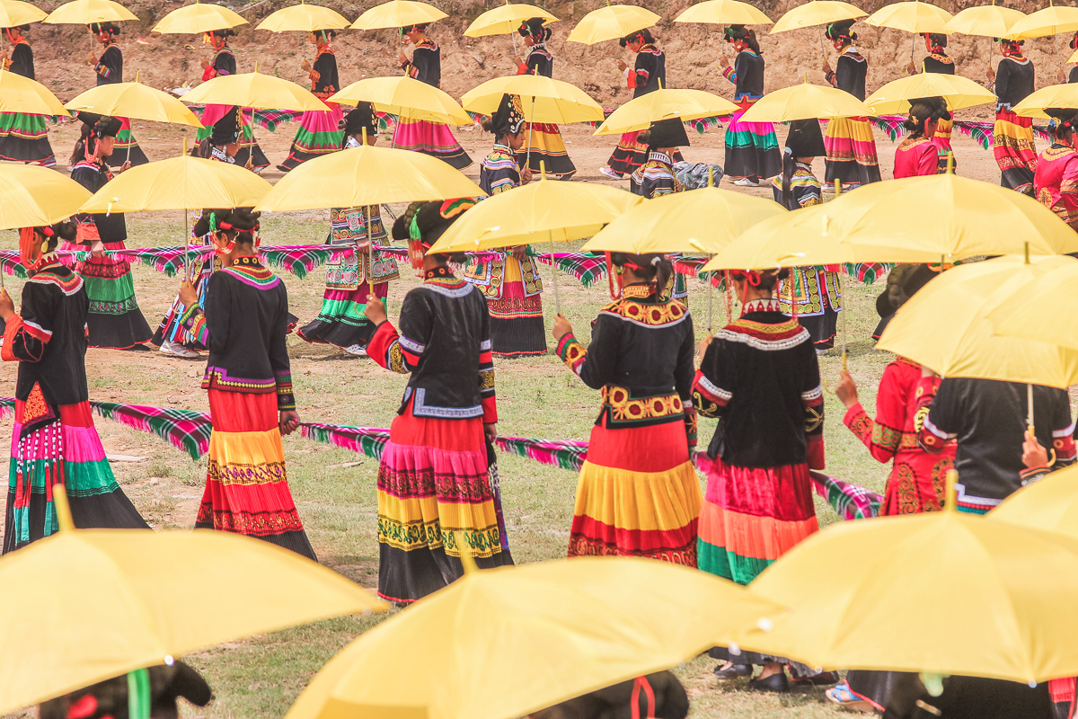Yi lopen met een gele paraplu tijdens een schoonheidswedstrijd van het festival in de omgeving van Xichang